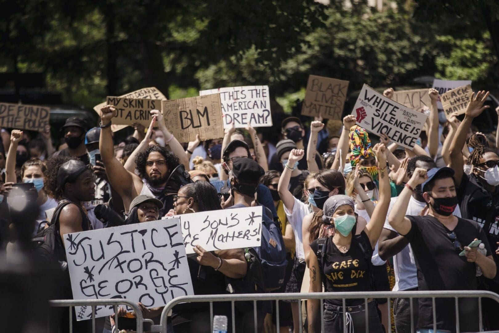 A crowd of people holding signs and standing next to a fence.