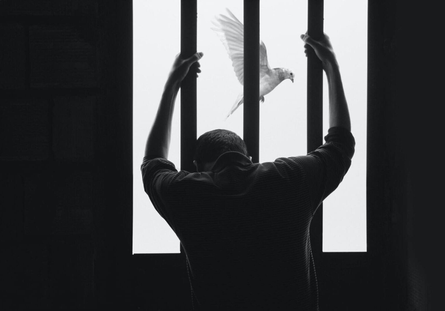 A man standing in front of bars with his arms raised up.